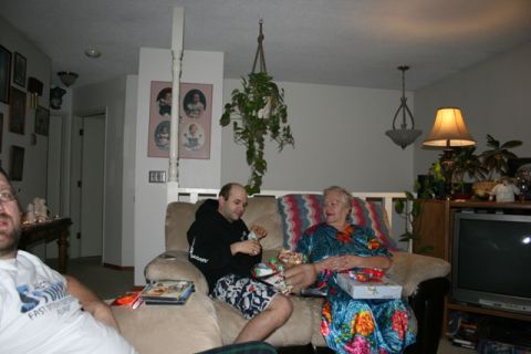 1990 Chevrolet Suburban - Two people are sitting on a couch in a living room, opening gifts. A man in a black hoodie and patterned shorts is on the left, and a woman…