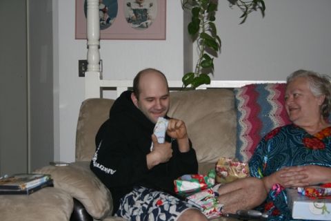 1990 Chevrolet Suburban - A man in a black hoodie and patterned shorts sits on a couch and opens a gift. A woman in a blue and red patterned robe sits next to him. T…