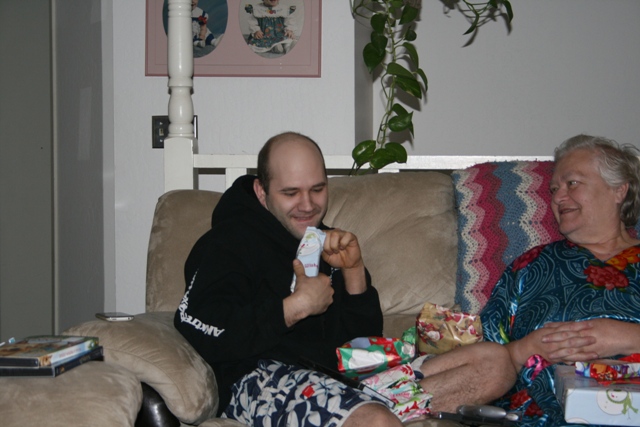 A man opens a gift on a couch next to a woman.