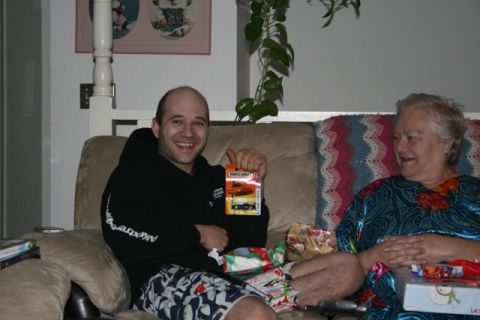 1990 Chevrolet Suburban - A smiling man holds up a Matchbox toy car while sitting on a couch next to an older woman. There are wrapped gifts on the couch.
