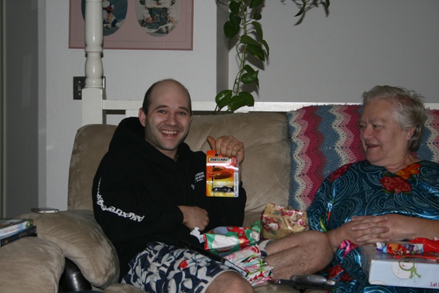 Man holding a Matchbox toy car, sitting on a couch with an older woman.