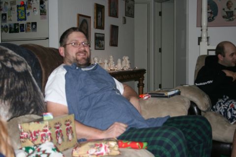 1990 Chevrolet Suburban - A man wearing glasses and a white t-shirt is sitting on a couch, holding a blue cloth. Presents are wrapped and placed on the couch in fron…