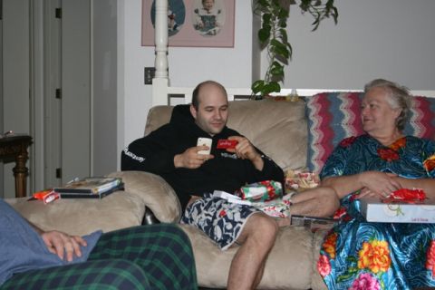 1990 Chevrolet Suburban - A man sits on a couch holding a smartphone and a red gift card while a woman sits next to him with wrapped presents.