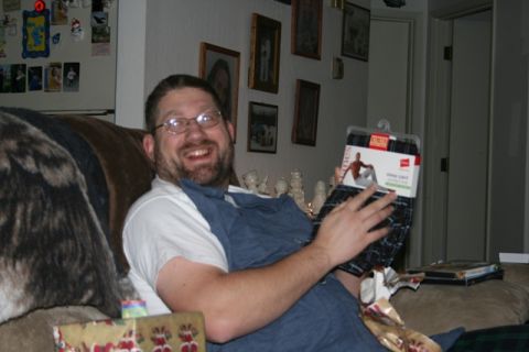 1990 Chevrolet Suburban - bearded man wearing glasses smiles on a sofa while opening a gift of plaid boxer shorts in a living room.