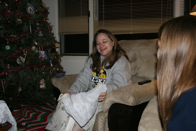 Woman unwrapping a gift next to a Christmas tree.