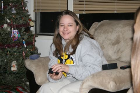 1990 Chevrolet Suburban - A woman sits on a couch next to a Christmas tree and holds a black object in her hands. She is wearing a gray hooded sweatshirt.