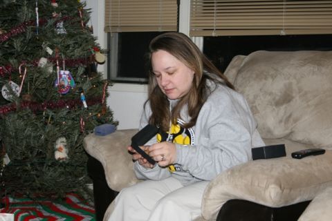 1990 Chevrolet Suburban - A woman sits on a couch next to a decorated Christmas tree and looks down at a small black object in her hands.