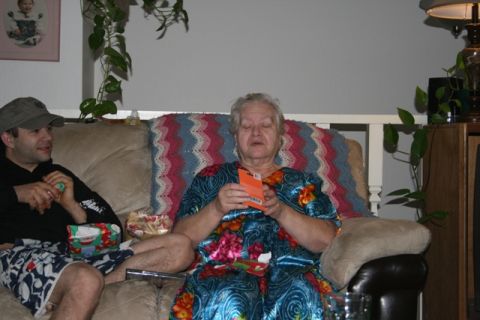 1990 Chevrolet Suburban - An older woman sits on a couch, looking at a small orange box in her hands. A younger man wearing a baseball cap sits to her left on the sa…