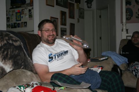 1990 Chevrolet Suburban - A man wearing glasses and a white t-shirt sits on a couch holding a silver object. He is smiling and looking towards the camera. Another ma…