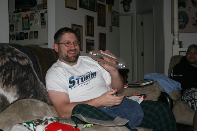 Man on couch holding a silver object, smiling at the camera.