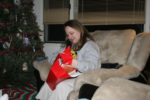 1990 Chevrolet Suburban - A woman sits on a couch next to a decorated Christmas tree, opening a red gift box.