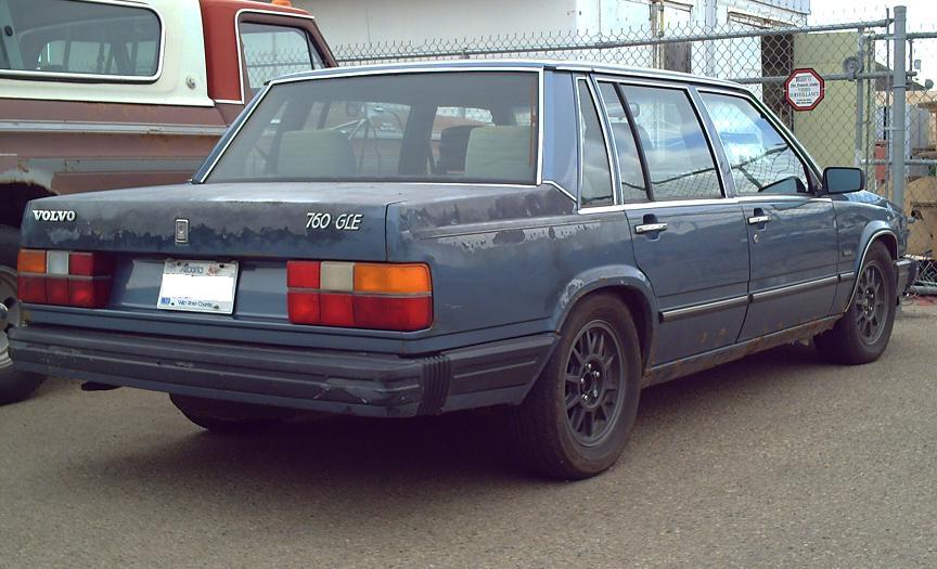 Weathered blue 1980s Volvo 760 GLE sedan, rear passenger side view.
