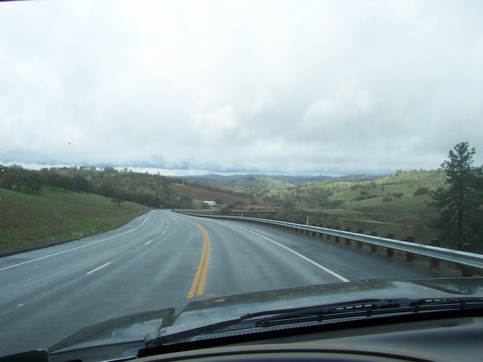 View from inside a vehicle driving on a wet highway through rolling hills.