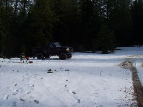 1994 Ford F-150 - A black Ford F-150 pickup truck is parked in a snowy wooded area next to some camping equipment. The truck has large off-road tires and is…