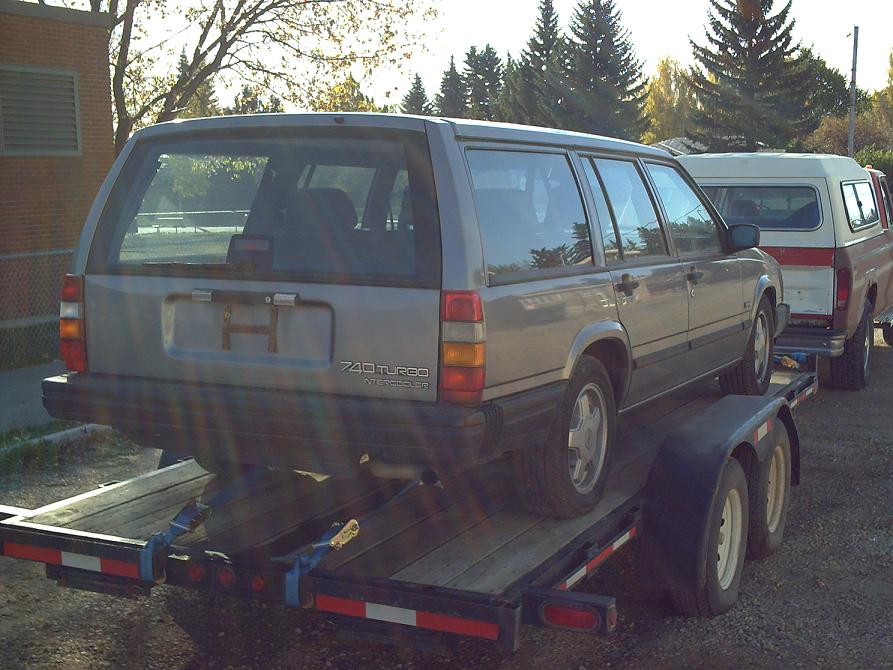 Silver Volvo 740 Turbo wagon loaded on a flatbed trailer, rear view.