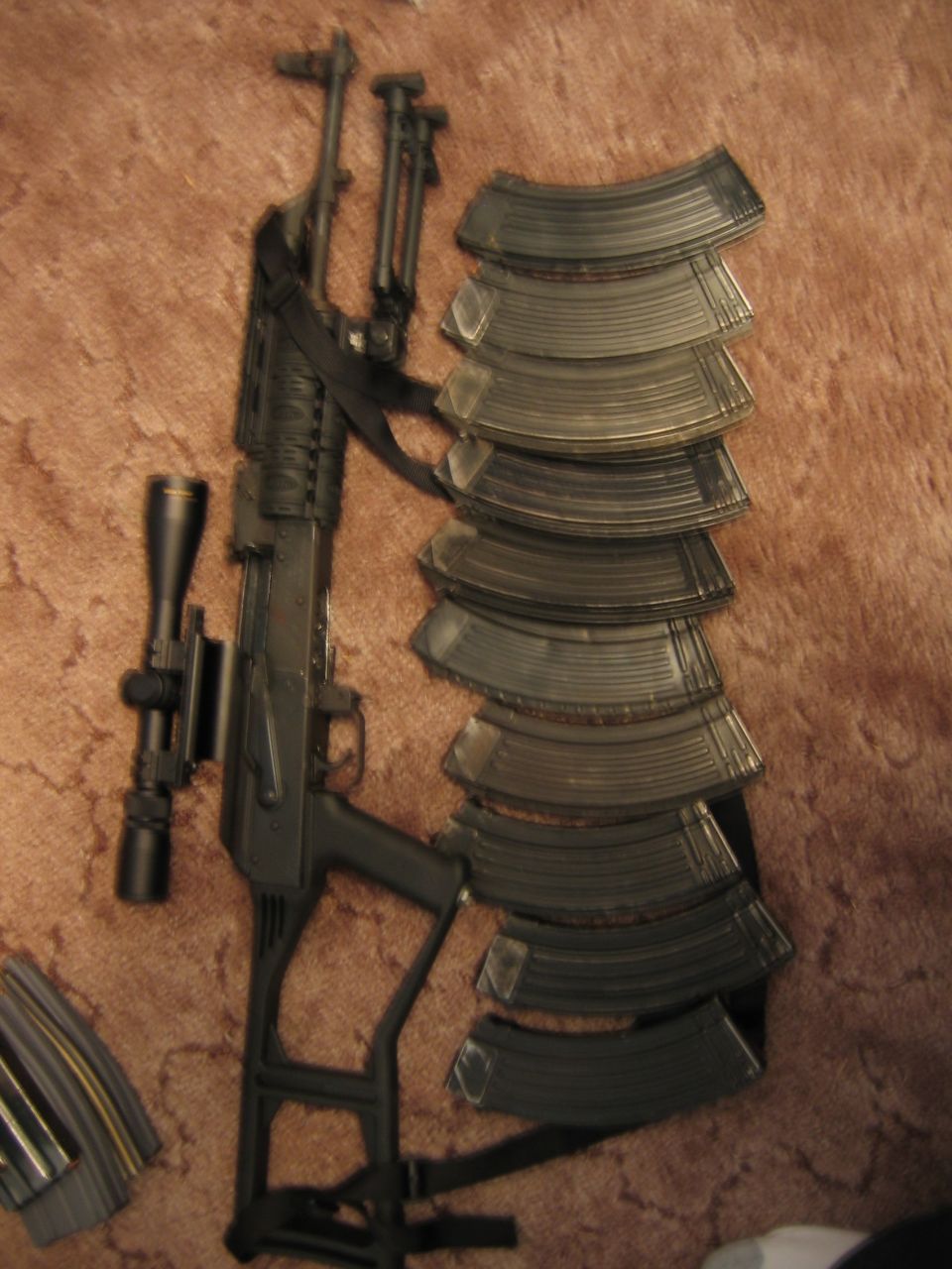 Rifle with scope and many magazines on a brown carpet.