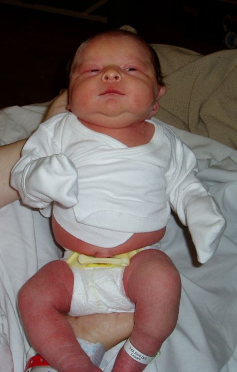 2000 Ford E350 - A newborn baby is held, wearing a white onesie and a diaper. The baby has red skin and a double chin.