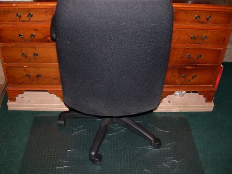 2000 Ford Crown Victoria - The image shows the back of a black office chair in front of a wooden dresser with multiple drawers. The chair is on a clear plastic floor…