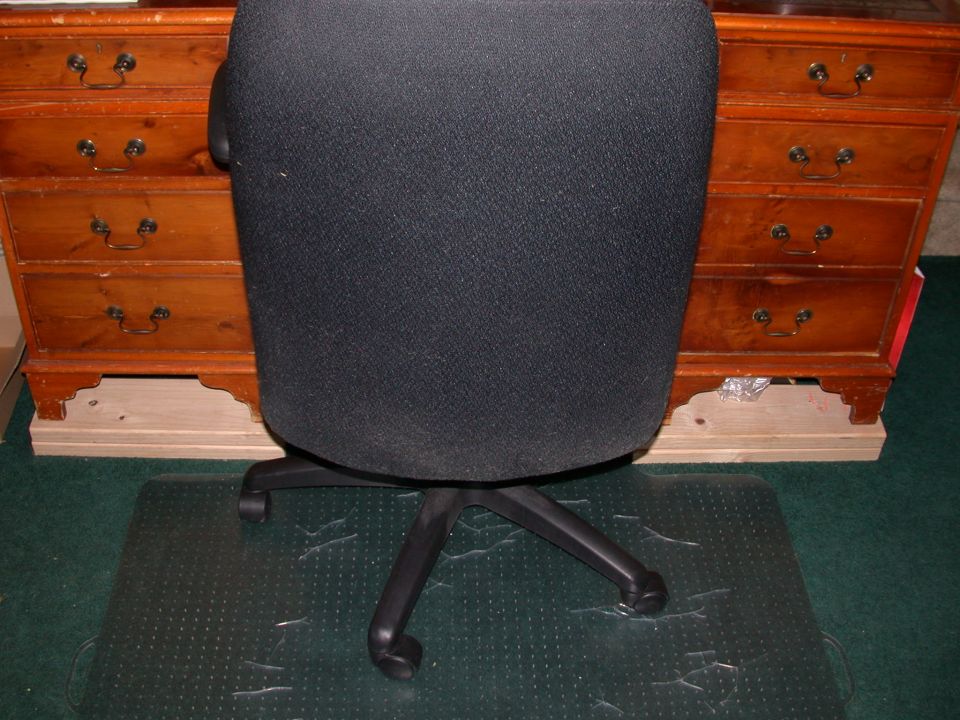 Black office chair in front of a wooden dresser on a clear floor mat
