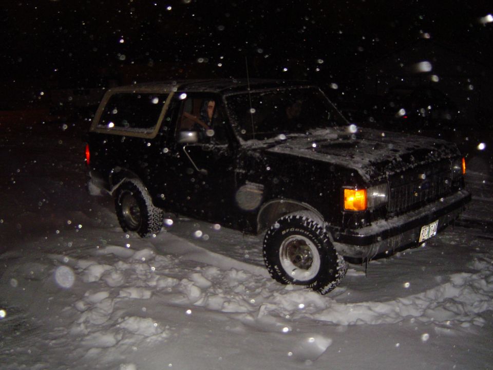 Dark lifted Ford Bronco on BFGoodrich mud tires driving through deep snow at night