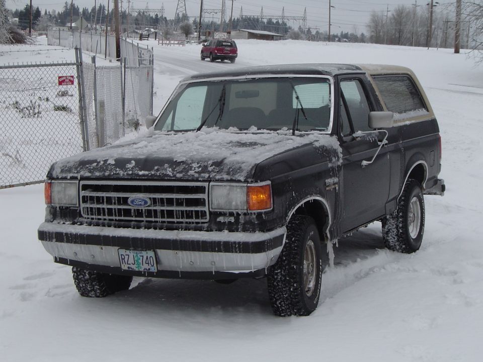 Snow-covered black Ford Bronco with tan top and Oregon plate, 3/4 front view