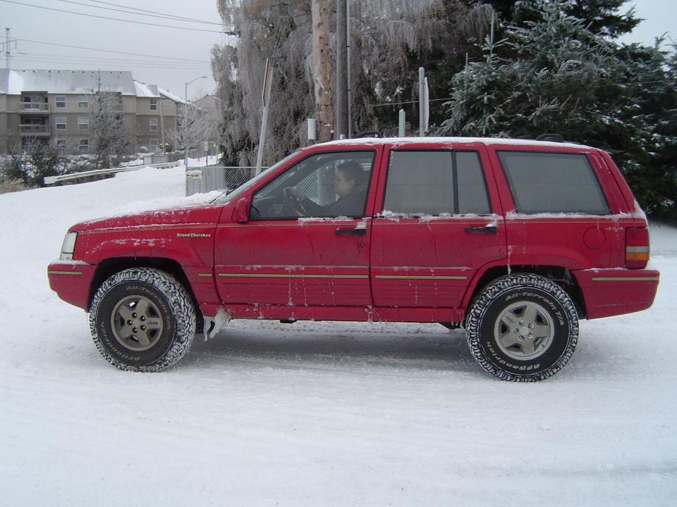Red Jeep Grand Cherokee ZJ in profile on a snow-covered road with BFGoodrich all-terrain tires