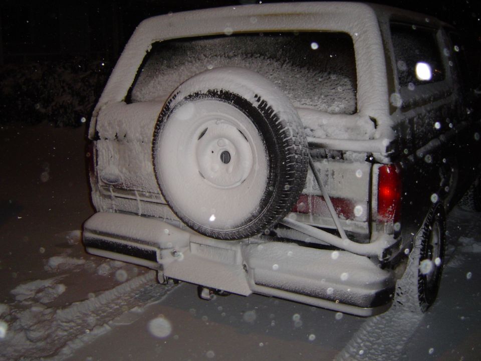 Snow-covered SUV at night from the rear with spare tire on a swing-out tailgate carrier