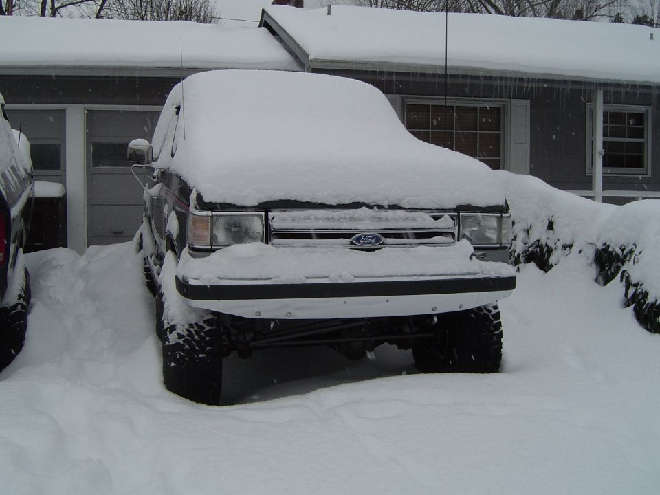 Lifted Ford truck covered in deep snow in a driveway, grille and Ford oval visible