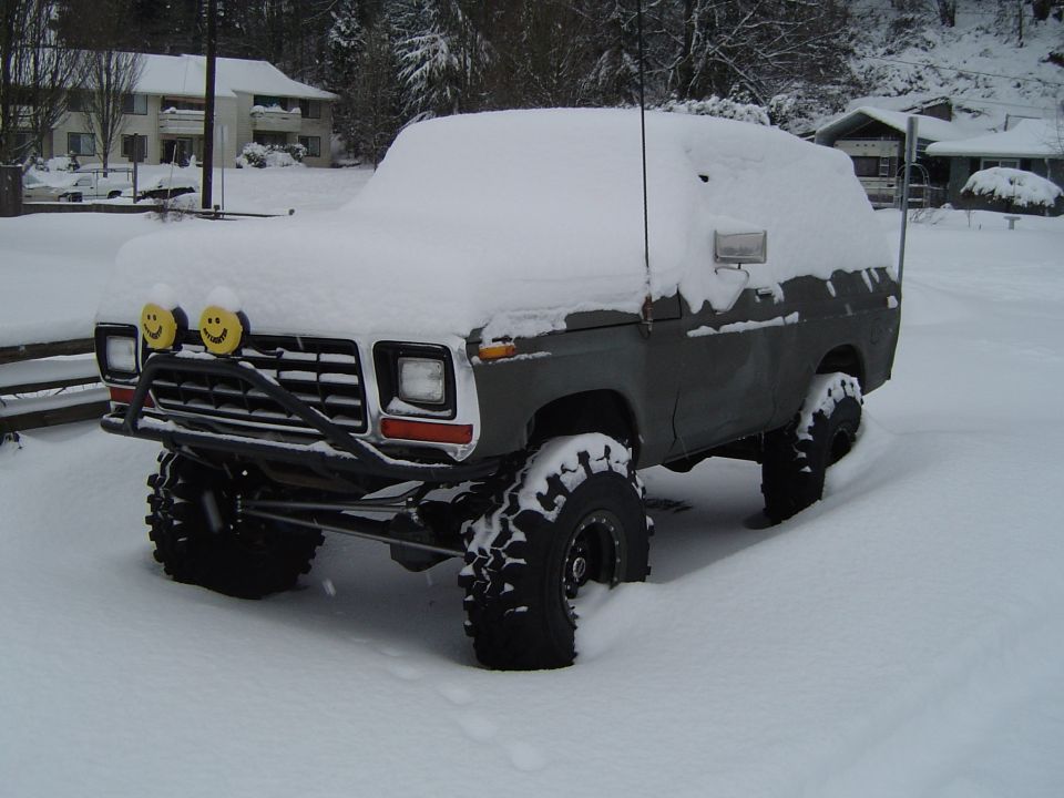 Lifted grey primered Ford Bronco covered in snow with yellow smiley-face light covers