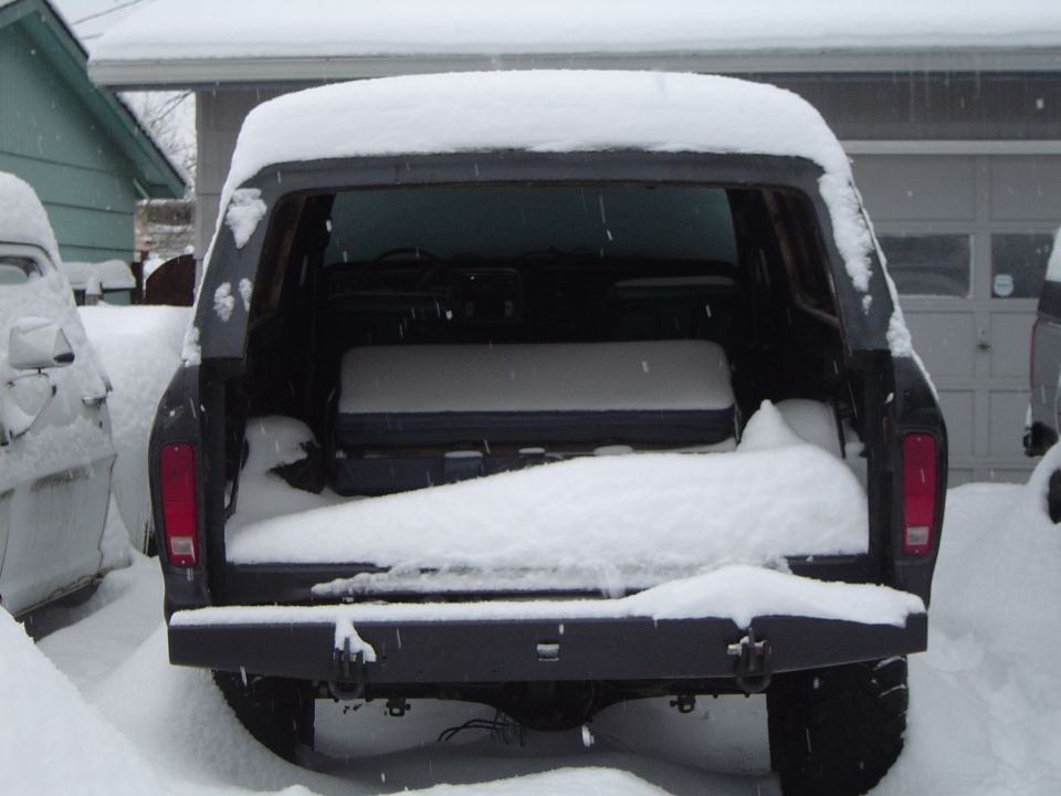 Snow-covered dark Ford Bronco with tailgate down showing gray rear bench seat