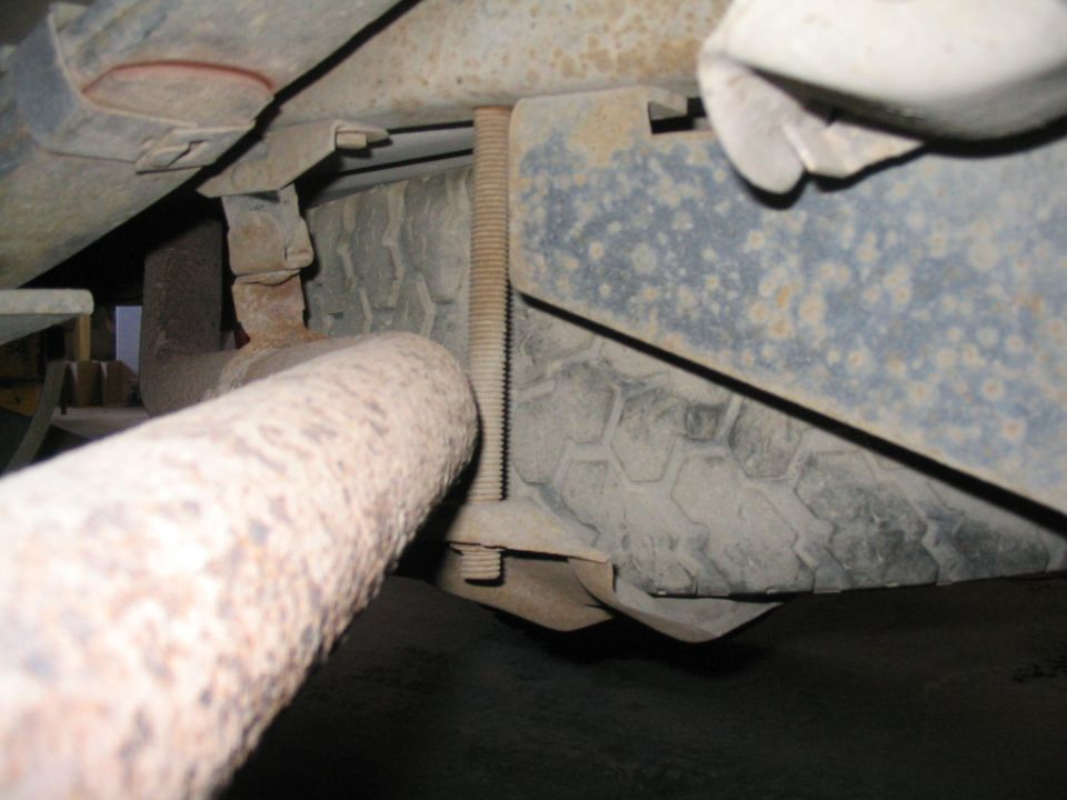 Underside of a vehicle showing a rusty exhaust pipe, spare tire, and suspension.