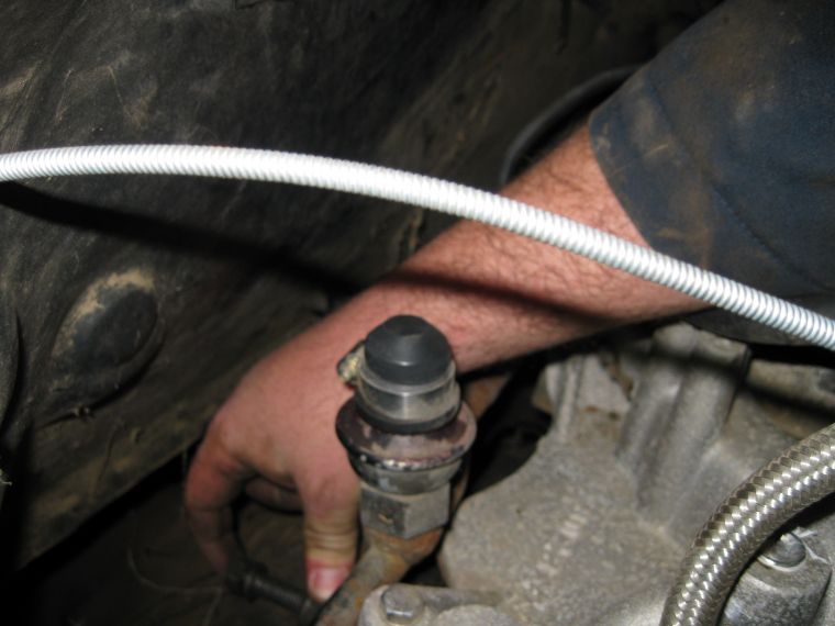 Close-up of a hand working on a vehicle's clutch master cylinder with a braided hose.