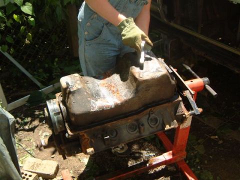 1982 Ford Bronco - An engine block sits on a stand as a person in overalls and gloves works on it outdoors.