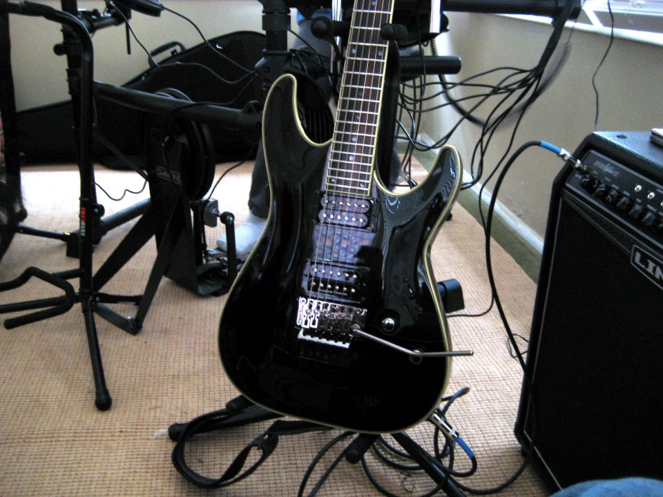 Black electric guitar on a stand connected to an amplifier with cables.