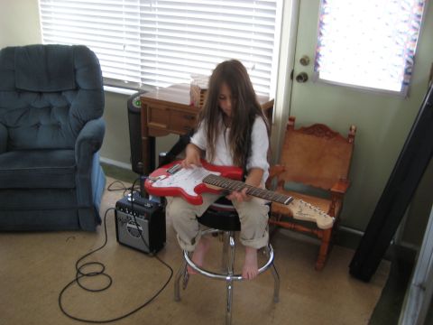 1996 Ford Bronco - A young girl sits on a stool playing a red electric guitar. She is connected to a small amplifier by a cable.