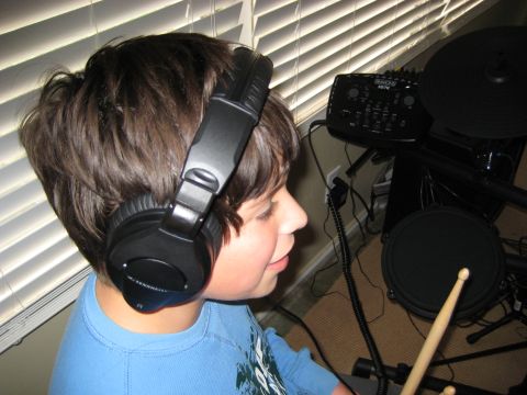 1996 Ford Bronco - A young person wearing headphones is looking towards a digital drum kit. The drum kit includes a control module, pads, and drumsticks.