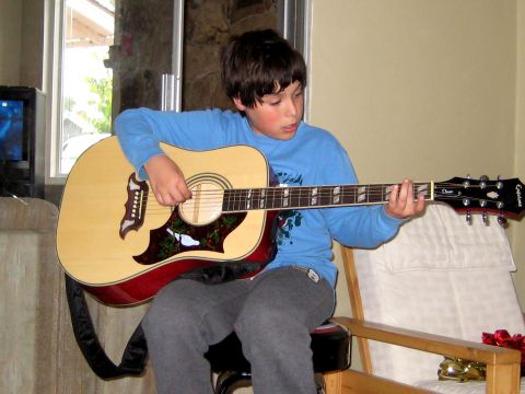 1996 Ford Bronco - A young boy is seated and playing an acoustic guitar indoors.