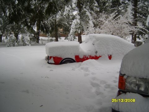 1989 Ford Bronco - A red vehicle is almost completely covered by snow, with only a portion of its side and wheel visible.