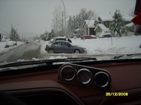 1989 Ford Bronco - A car is stuck in the snow on a street with houses in the background.