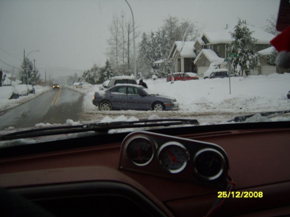 car stuck in snow on residential street, houses and trees covered in snow