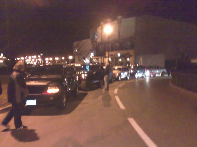 Several SUVs and trucks parked in a line at night, with people walking around