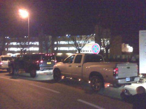 1991 Ford Crown Victoria - A white pickup truck is seen from the rear at night, with other vehicles and buildings in the background.