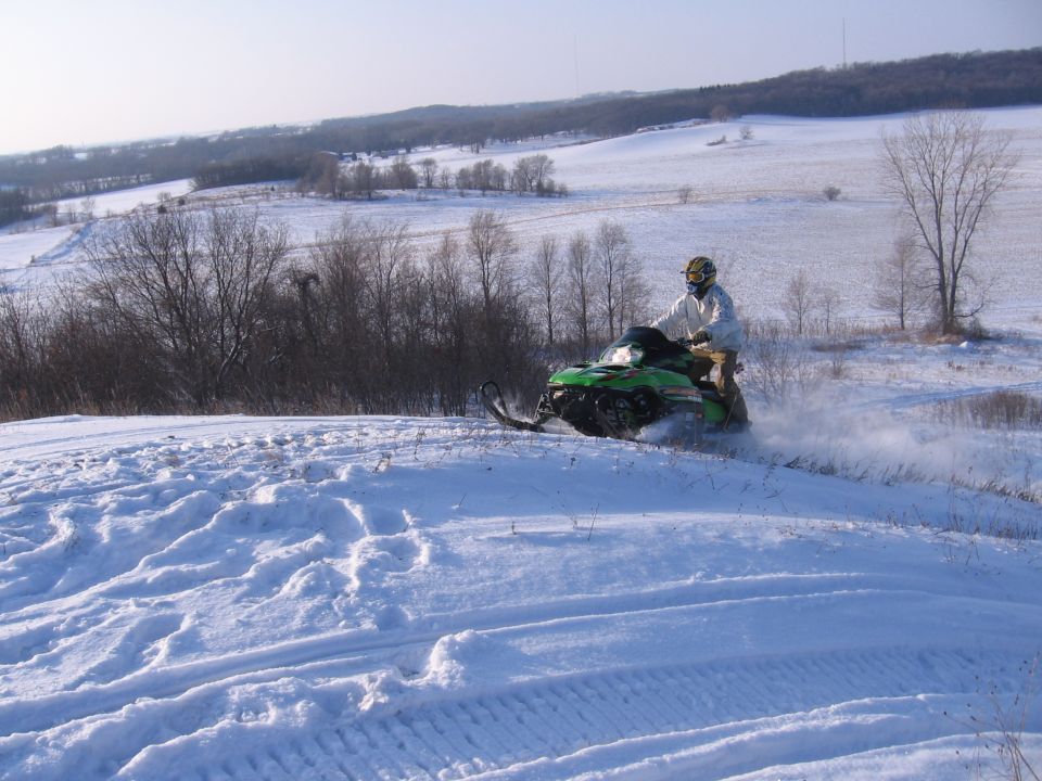 Rider on green snowmobile riding across snowy open field