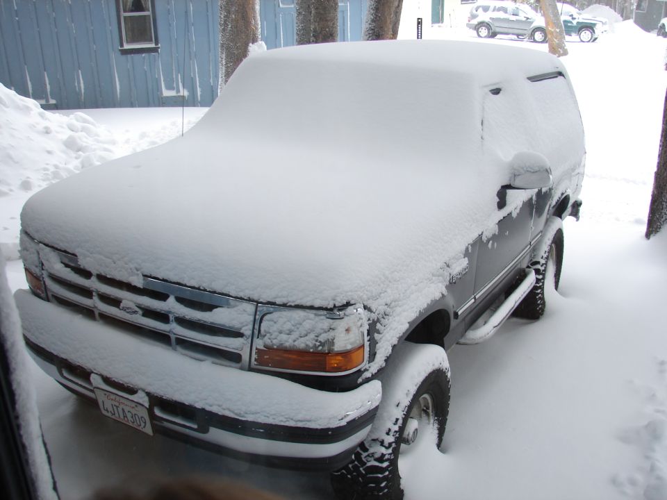 Snow-covered Ford pickup truck parked beside blue building