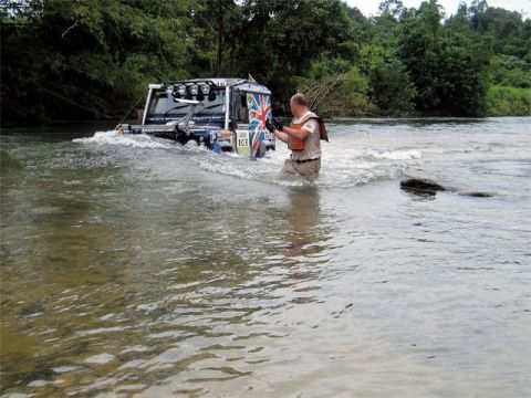 1991 Ford Bronco - A modified off-road vehicle navigates through a river, with a man in a life vest accompanying it on foot.