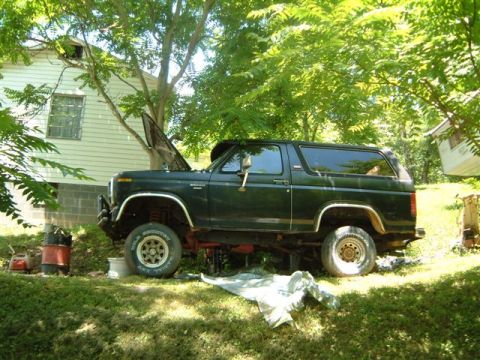1982 Ford Bronco - A dark green Ford Bronco sits in a grassy yard with its hood open, appearing to be worked on.