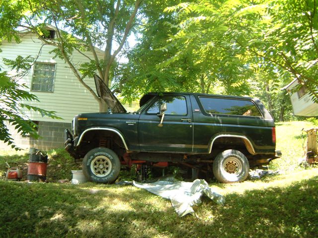 Dark green Ford Bronco parked in a yard with hood up, undergoing maintenance