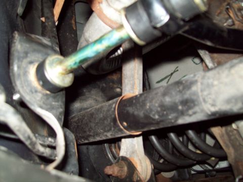 1999 Mercury Grand Marquis - Close underbody shot of a rear suspension showing a new gold-zinc sway bar end link with black boot bushings installed against the axle hou…
