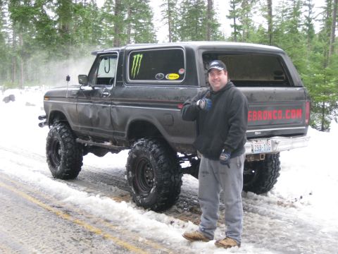 1979 Ford Bronco - A man stands beside a lifted black 1979 Ford Bronco on a snowy road, displaying its off-road capabilities.