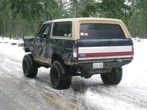1979 Ford Bronco - Rear view of a lifted Ford Bronco driving on a snowy road.